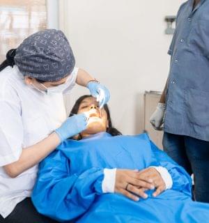 General Dentistry Indian woman dentist examining the mouth of a patient with the assistance of a male nurse